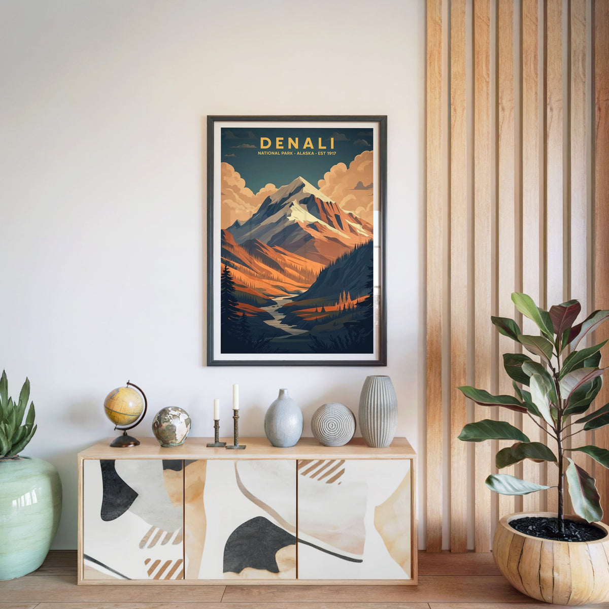 Denali National Park print in a black frame above a light wood sideboard with a globe and vases