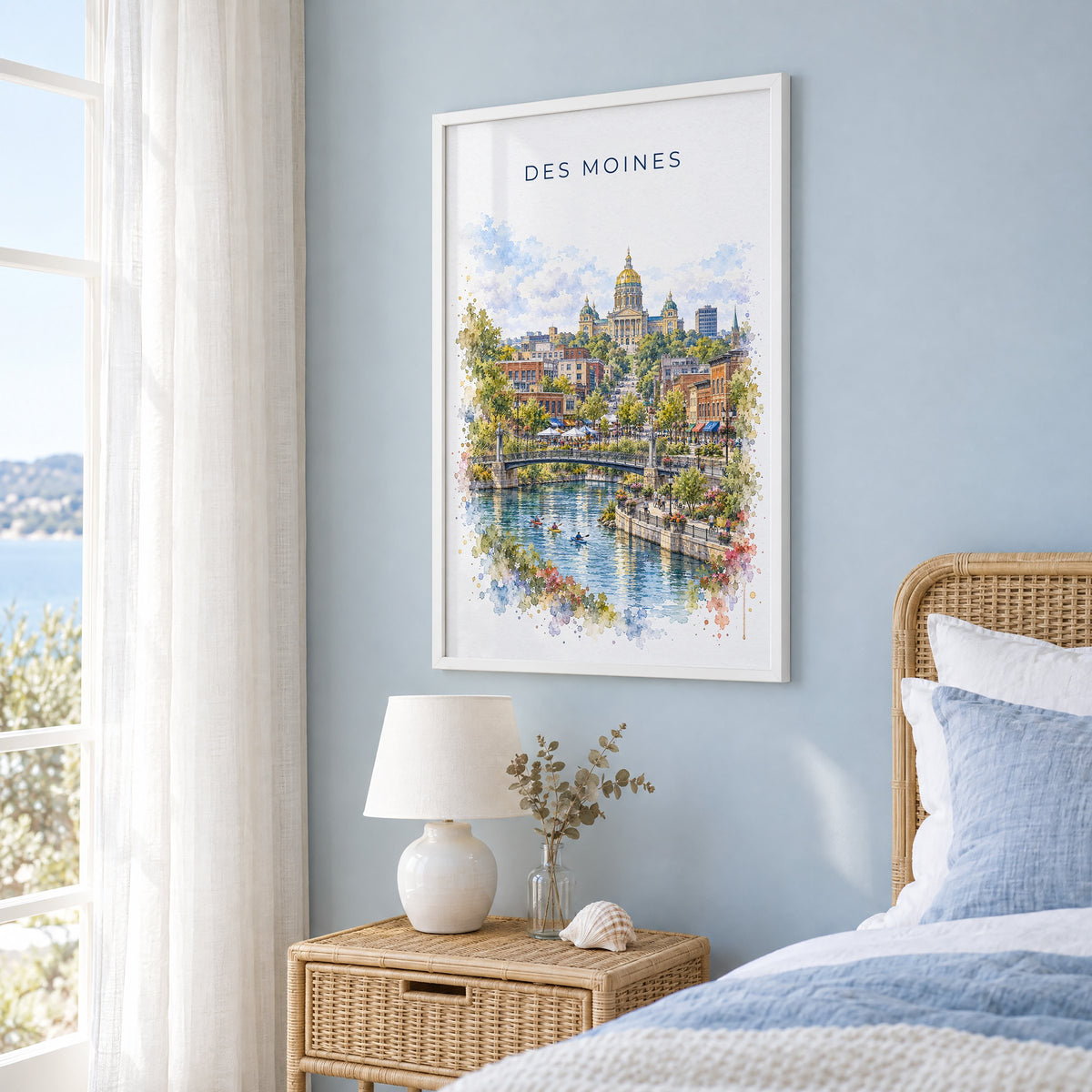 Des Moines watercolor print in a white frame on a pale blue wall beside a rattan bed in a coastal bedroom