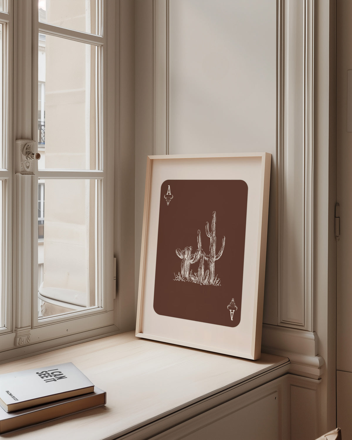 Desert cactus card print in a pale wood frame on a sunlit window ledge