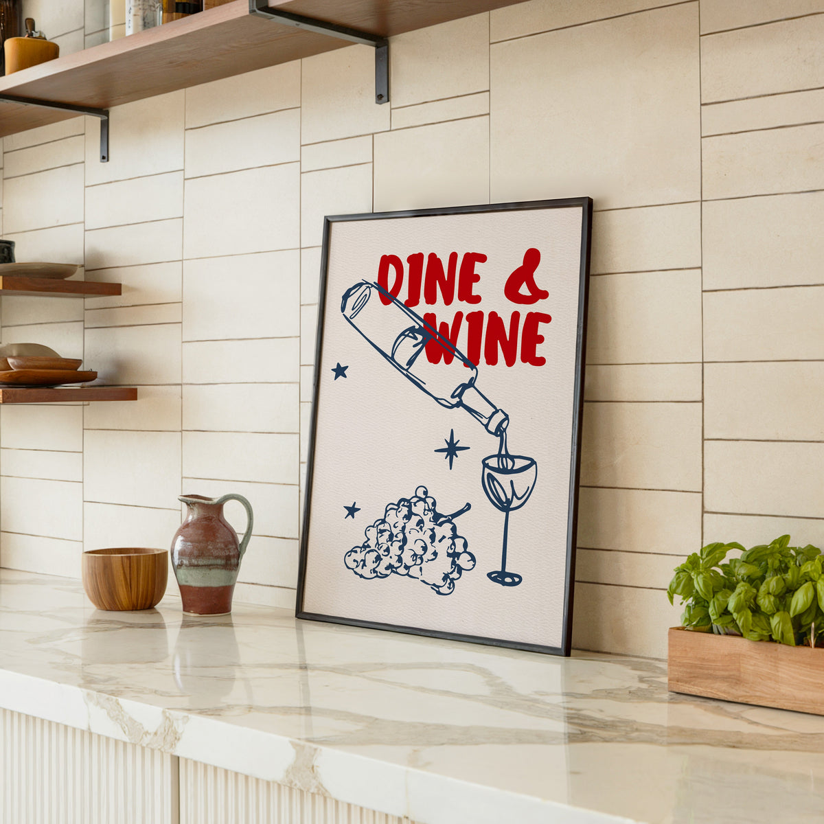 Dine and Wine print in a black frame leaning on a marble counter in a tiled kitchen