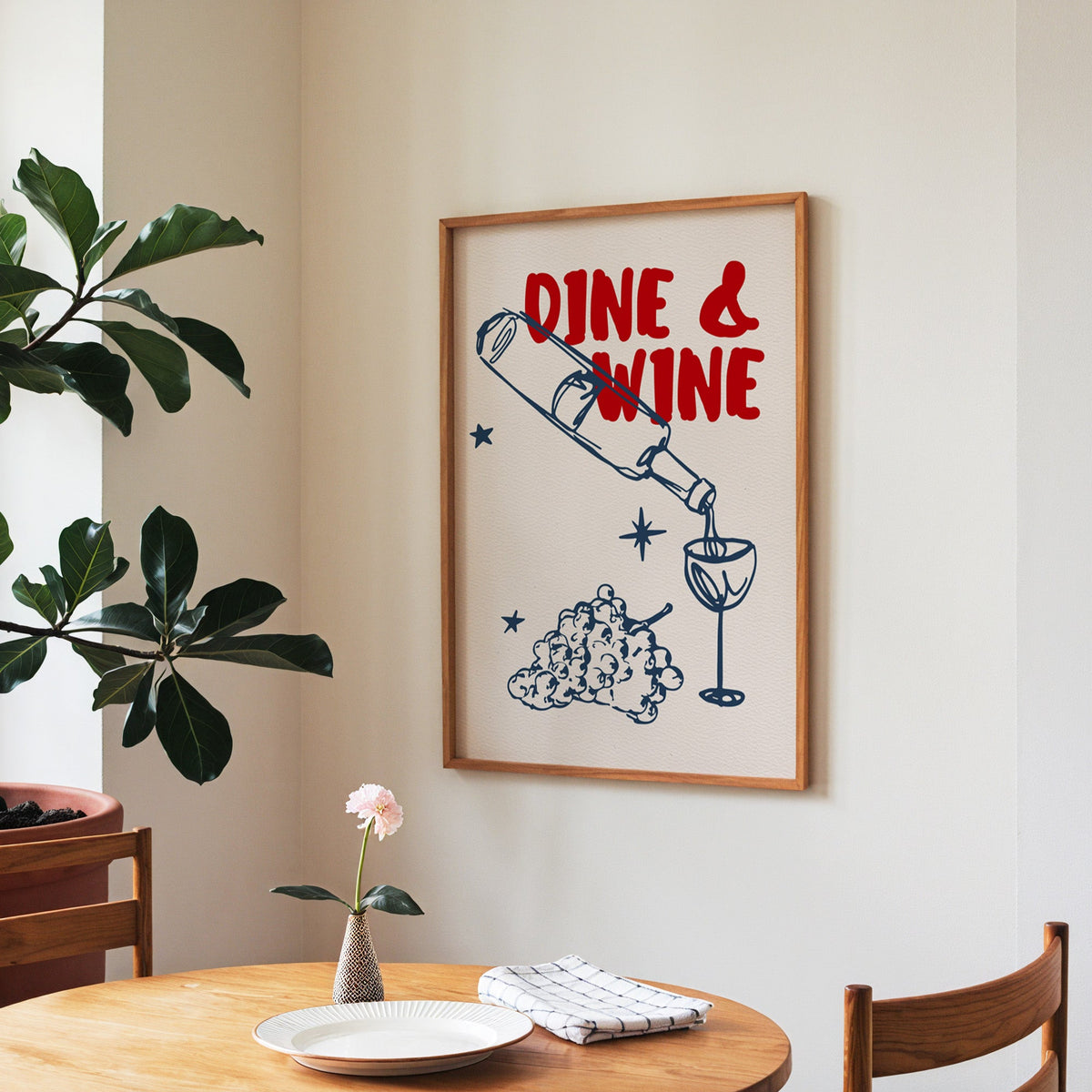 Dine and Wine print in a walnut frame above a round table beside a fiddle-leaf fig