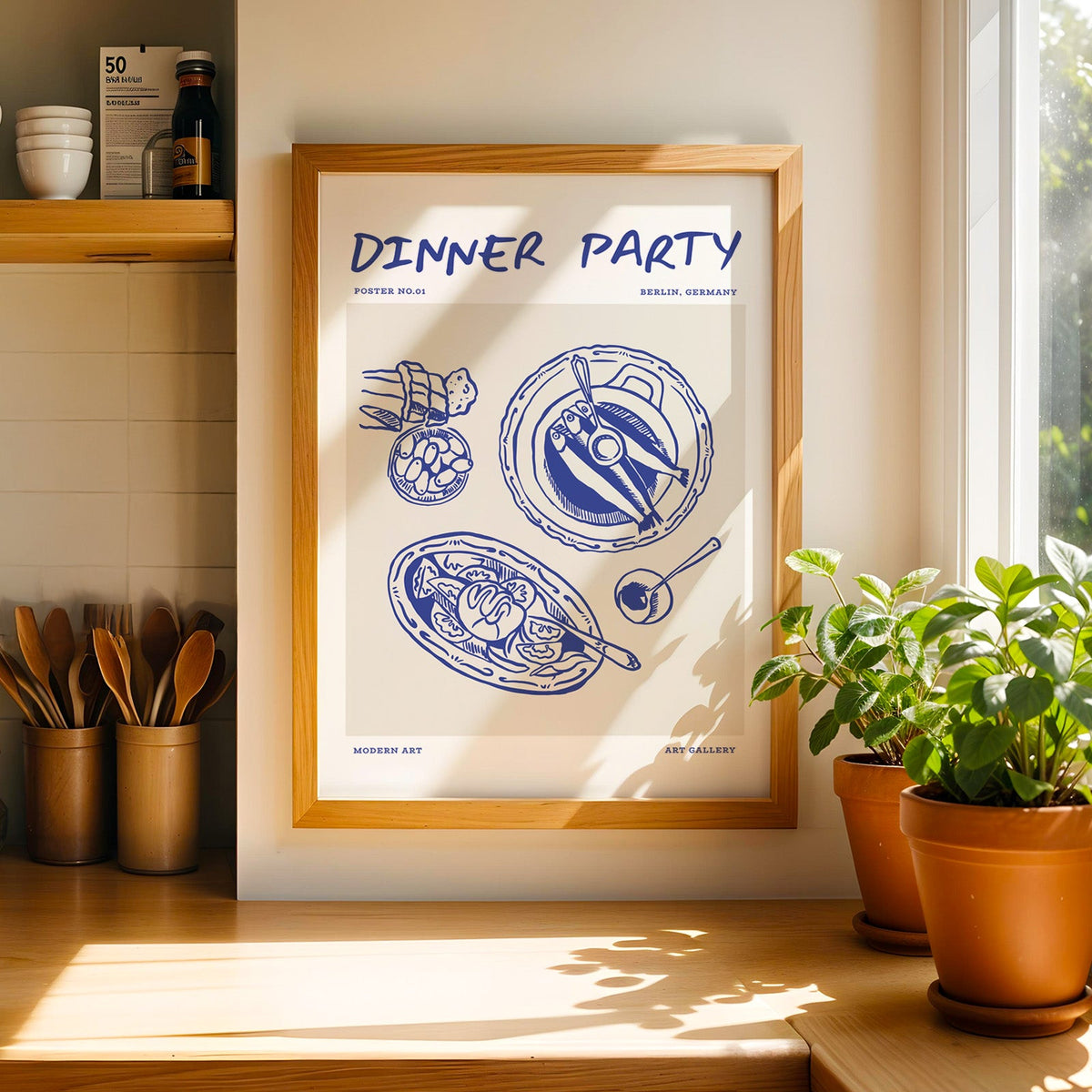 Dinner Party fish platters print in a light pine frame beside a jar of wooden spoons