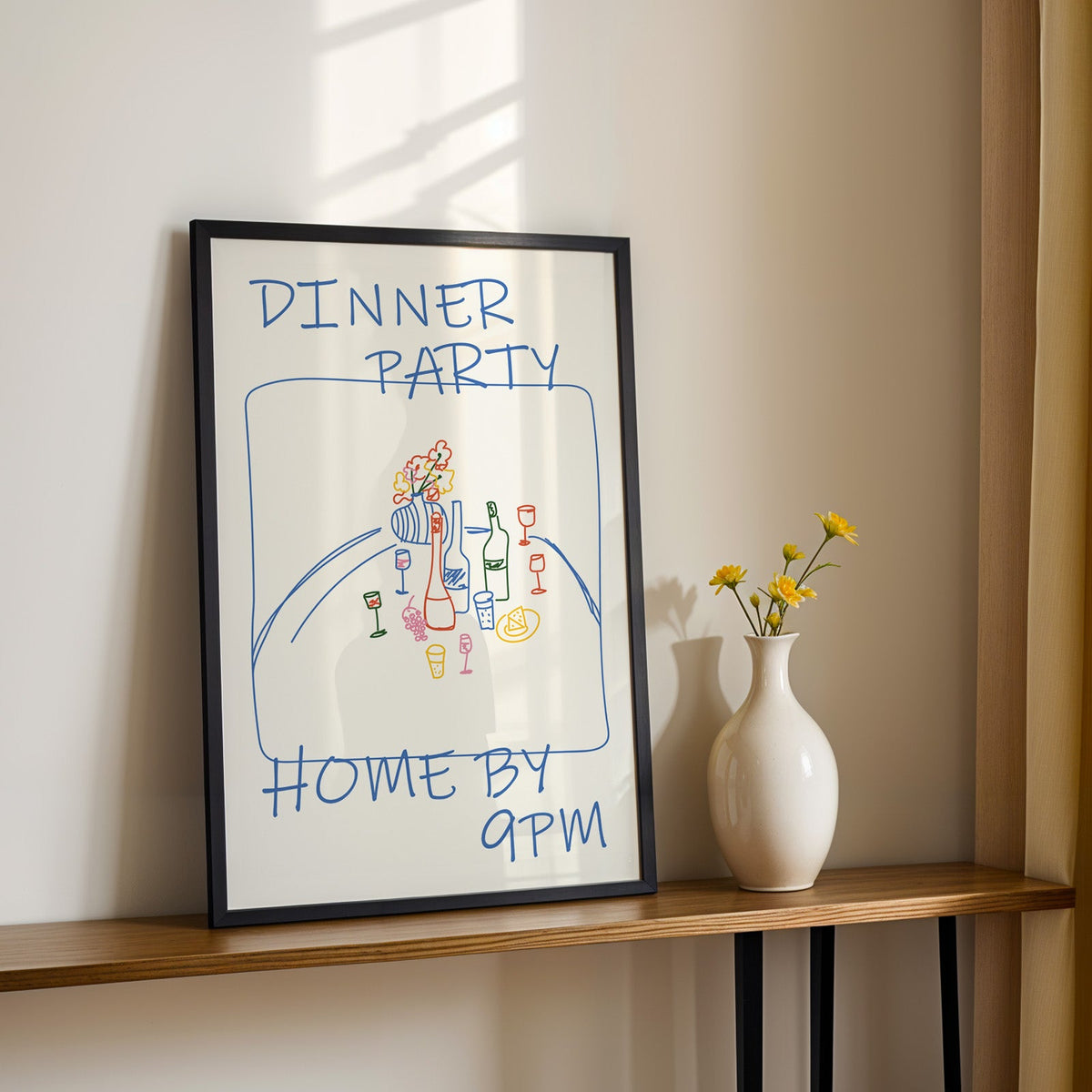 Dinner party blue line print in a black frame on a console table with yellow daisies