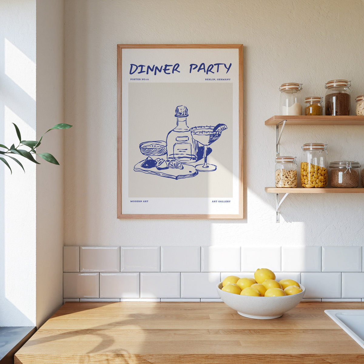 Dinner Party margarita print in an oak frame beside open kitchen shelves