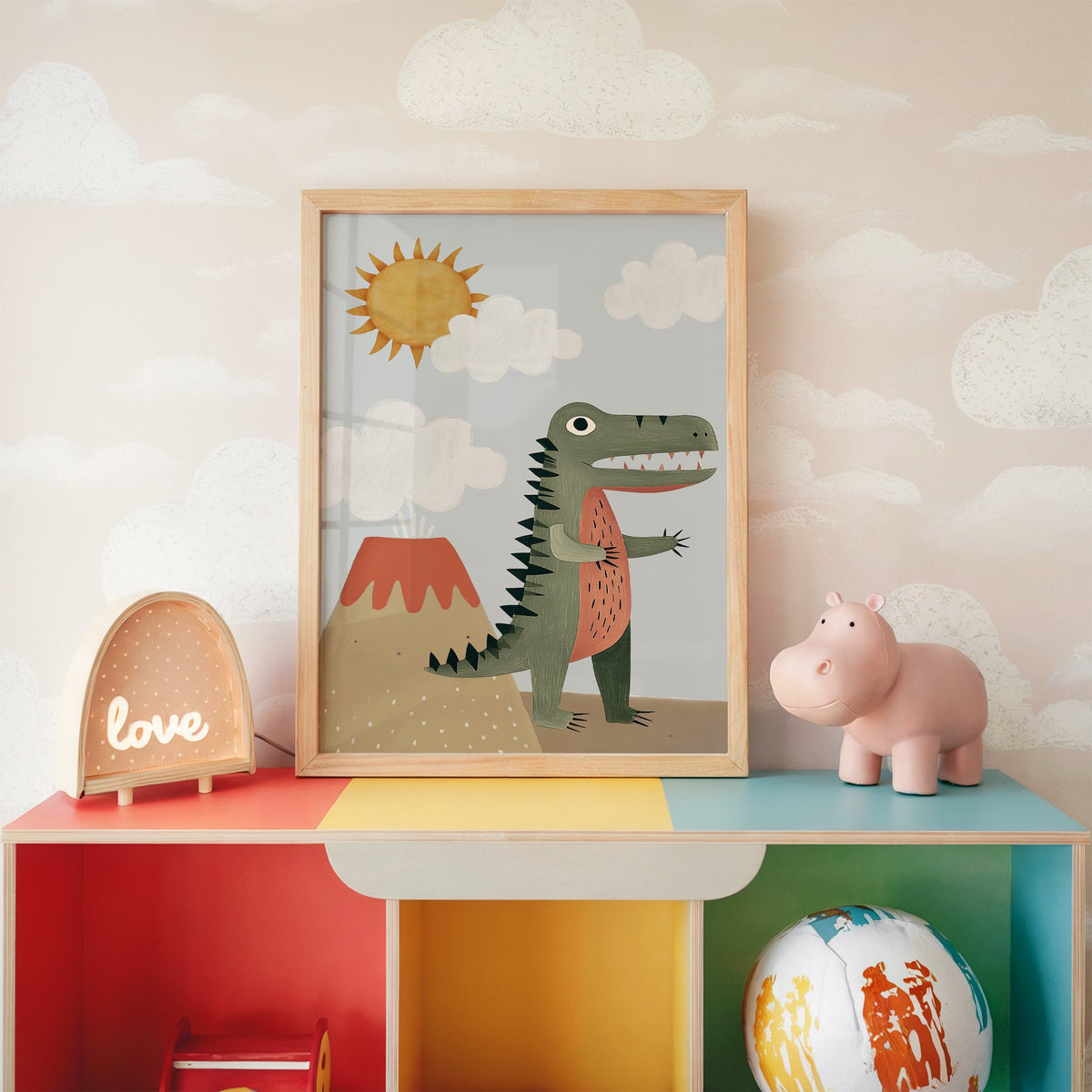 Dinosaur and volcano nursery print in an oak frame on a rainbow toy shelf against cloud wallpaper