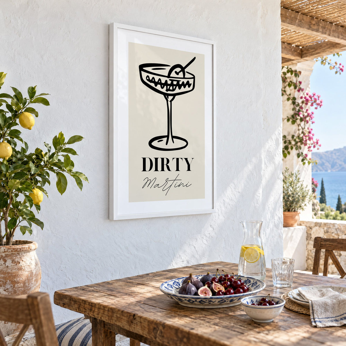 DIRTY Martini black line coupe olive print in a white frame on a whitewashed terrace wall above a lunch table with figs and cherries, seen at an angle
