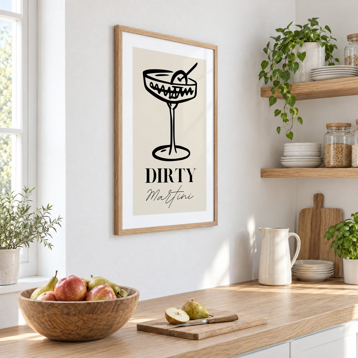 DIRTY Martini black line coupe olive print in an oak frame on a white kitchen wall above a counter with apples and pears, seen at an angle