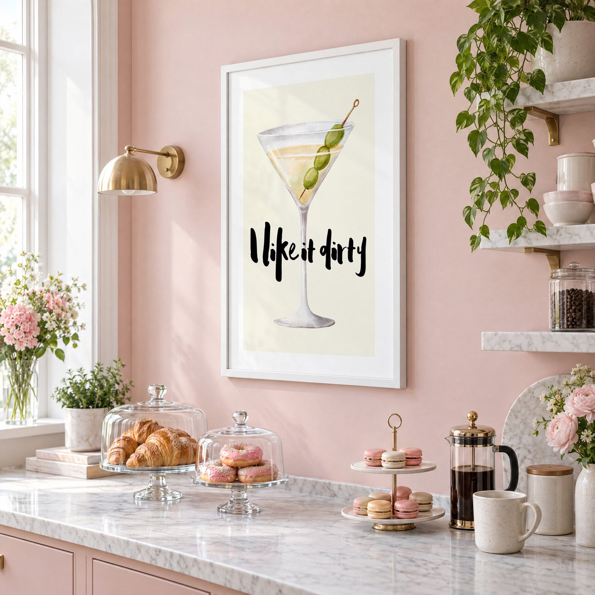 I like it dirty watercolor martini print in a white frame on a blush pink wall above a patisserie counter with croissants and macarons, seen at an angle