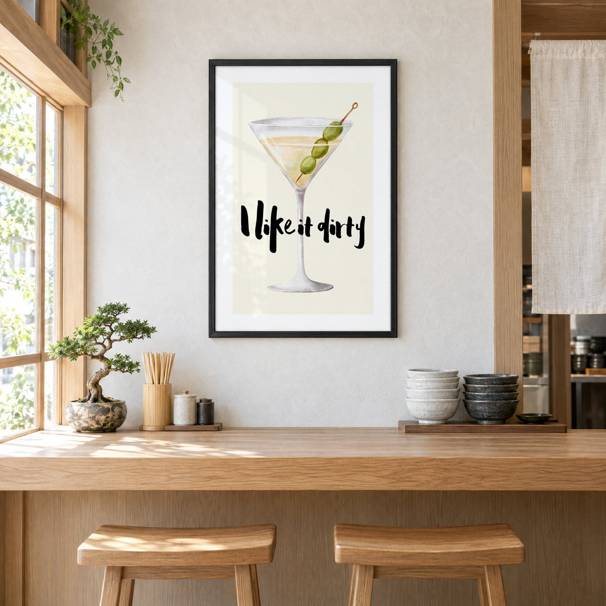I like it dirty watercolor martini print in a black frame above a light wood ramen counter with stools and stacked bowls
