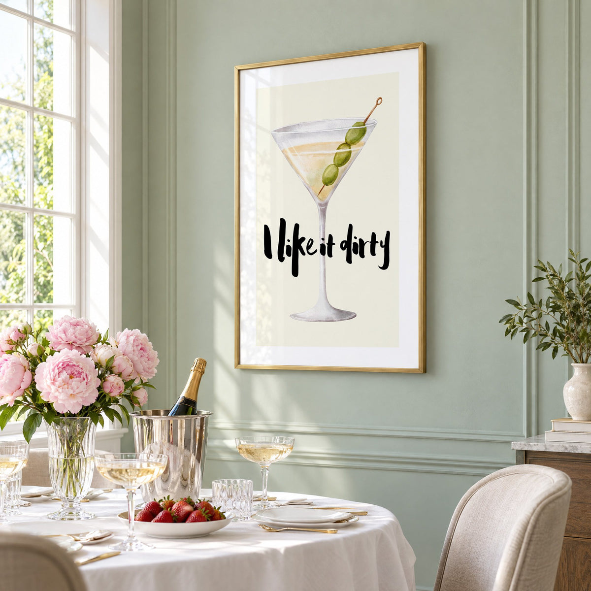 I like it dirty watercolor martini print in a brass frame on a sage wall above a brunch table with champagne and peonies, seen at an angle