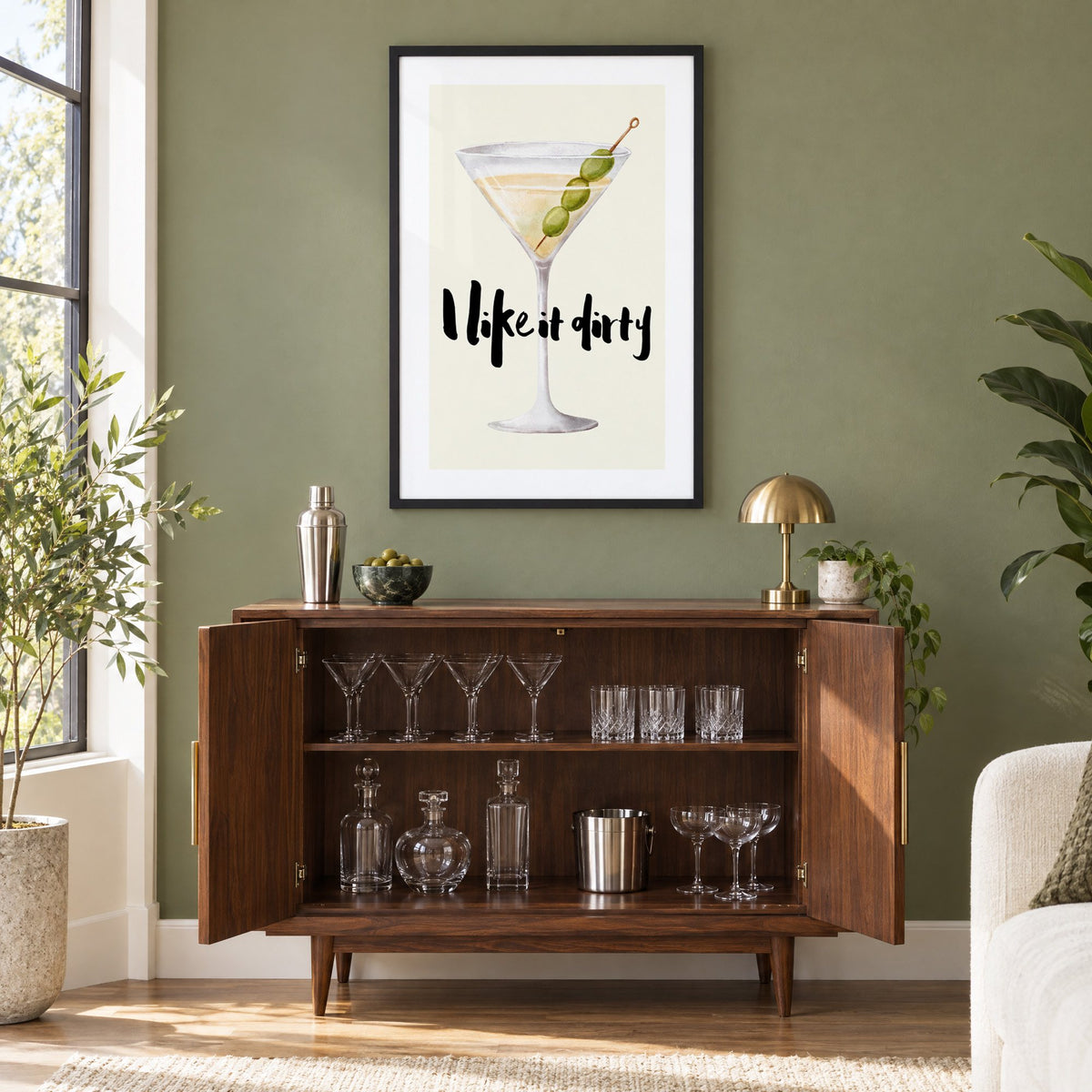 I like it dirty watercolor martini print in a black frame on an olive green wall above a walnut bar cabinet with glassware