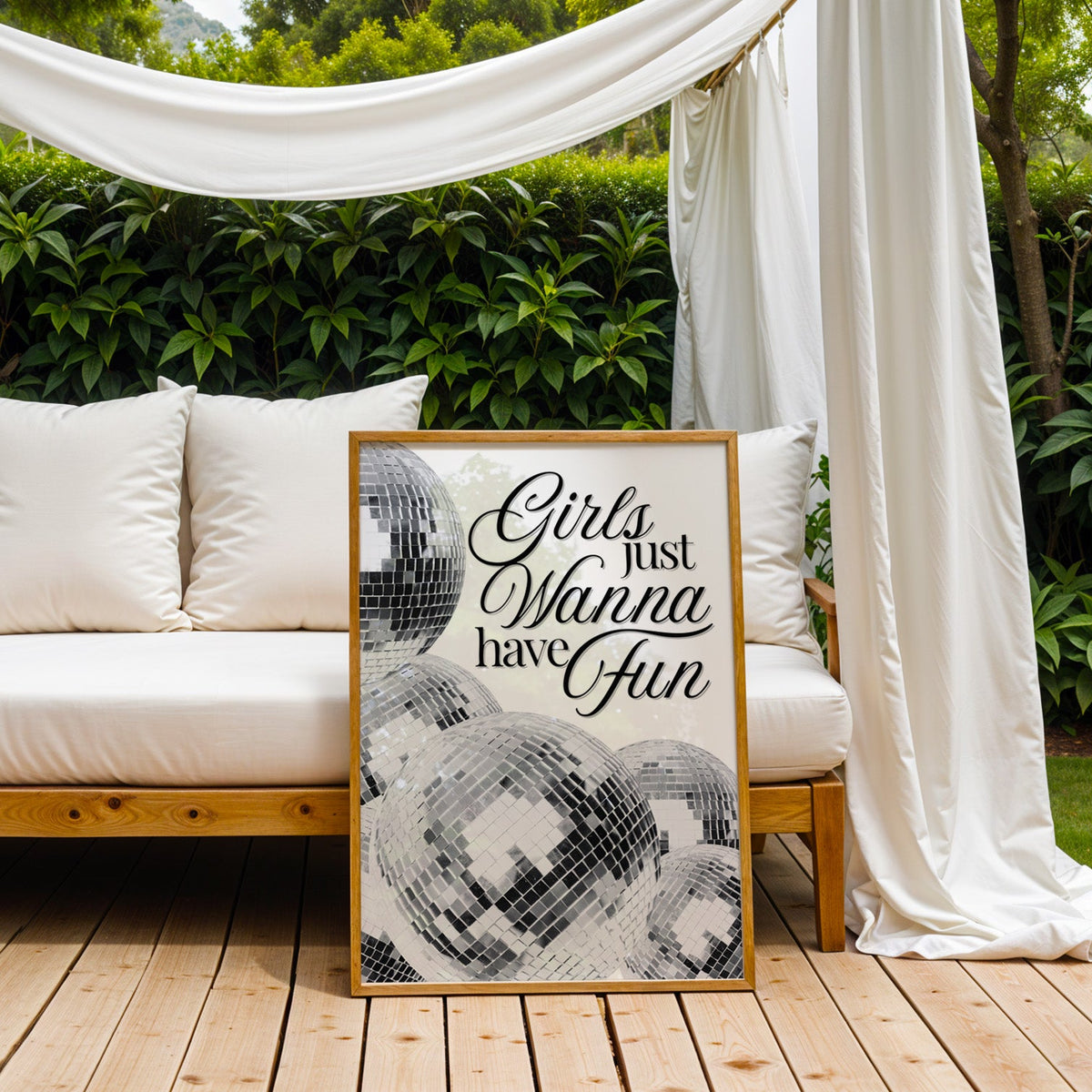 Disco balls with Girls just wanna have fun text print in an oak frame on an outdoor daybed under white drapes