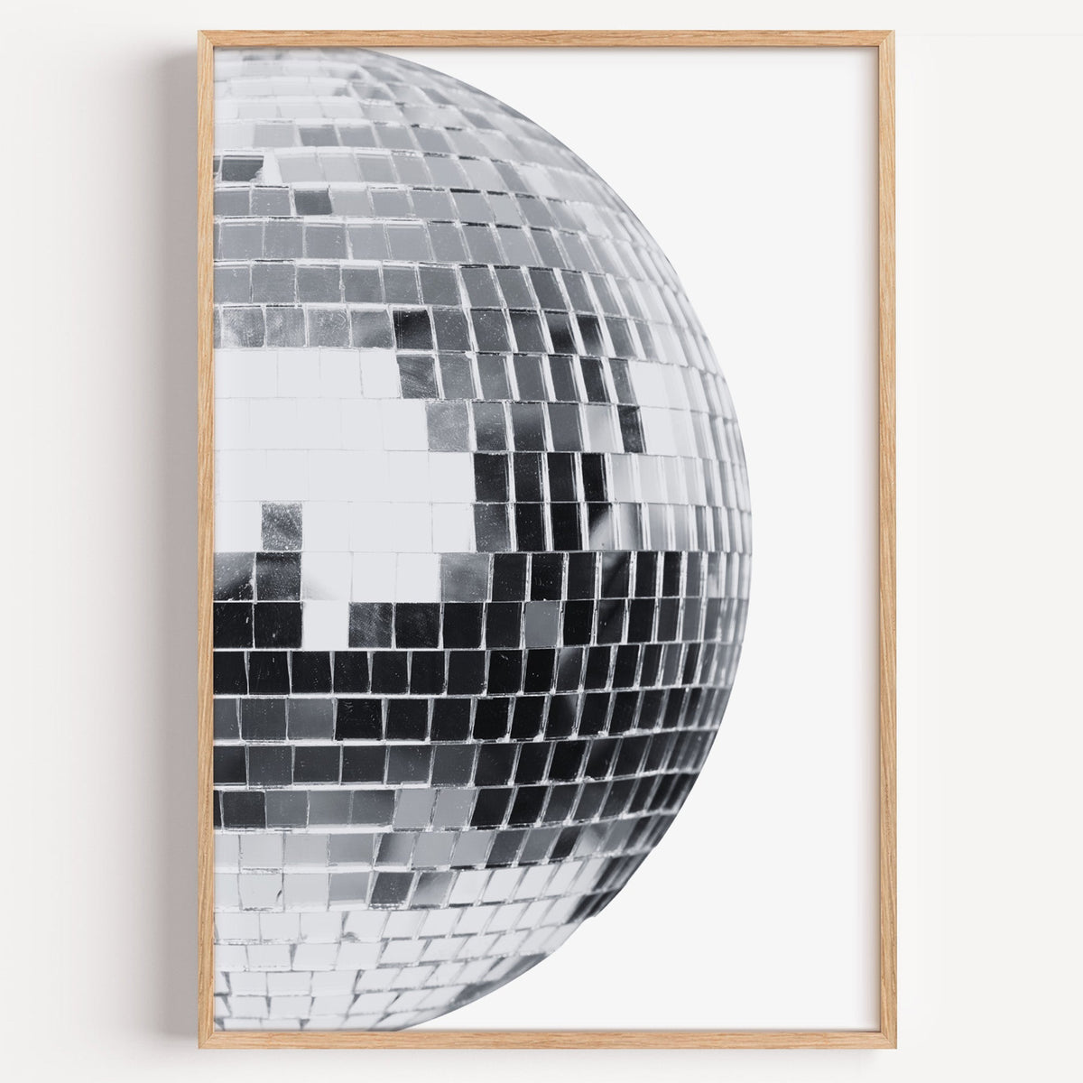 Disco mirror ball close-up print in a light oak frame on a plain white wall