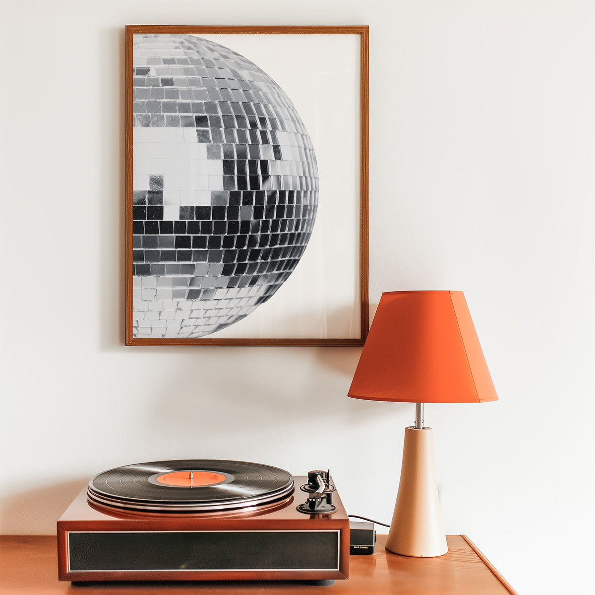 Disco mirror ball close-up print in a walnut frame above a record player and orange lamp