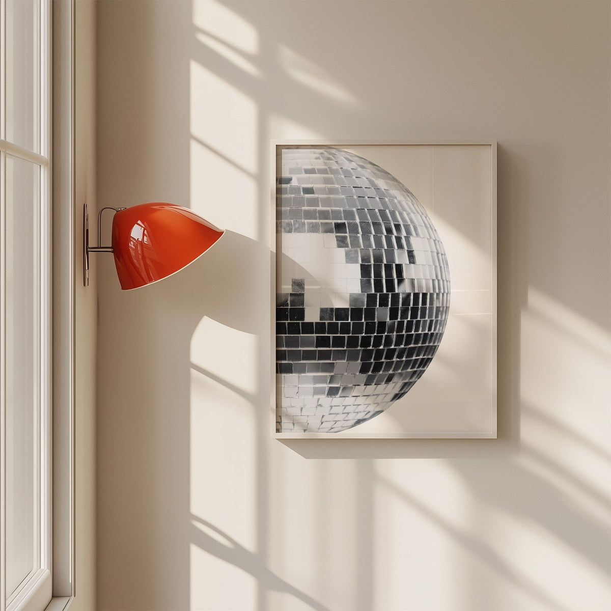 Disco mirror ball close-up print in a white frame on a sunlit wall beside a red sconce