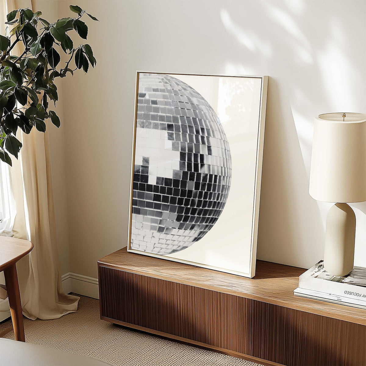 Disco mirror ball close-up print in a white frame on a walnut sideboard beside a ceramic lamp