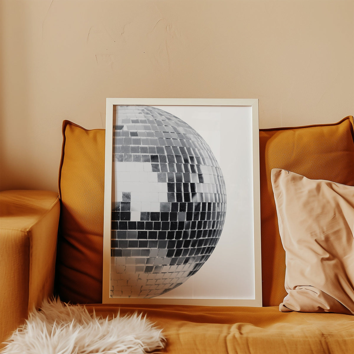 Disco mirror ball close-up print in a white frame leaning on a mustard velvet sofa