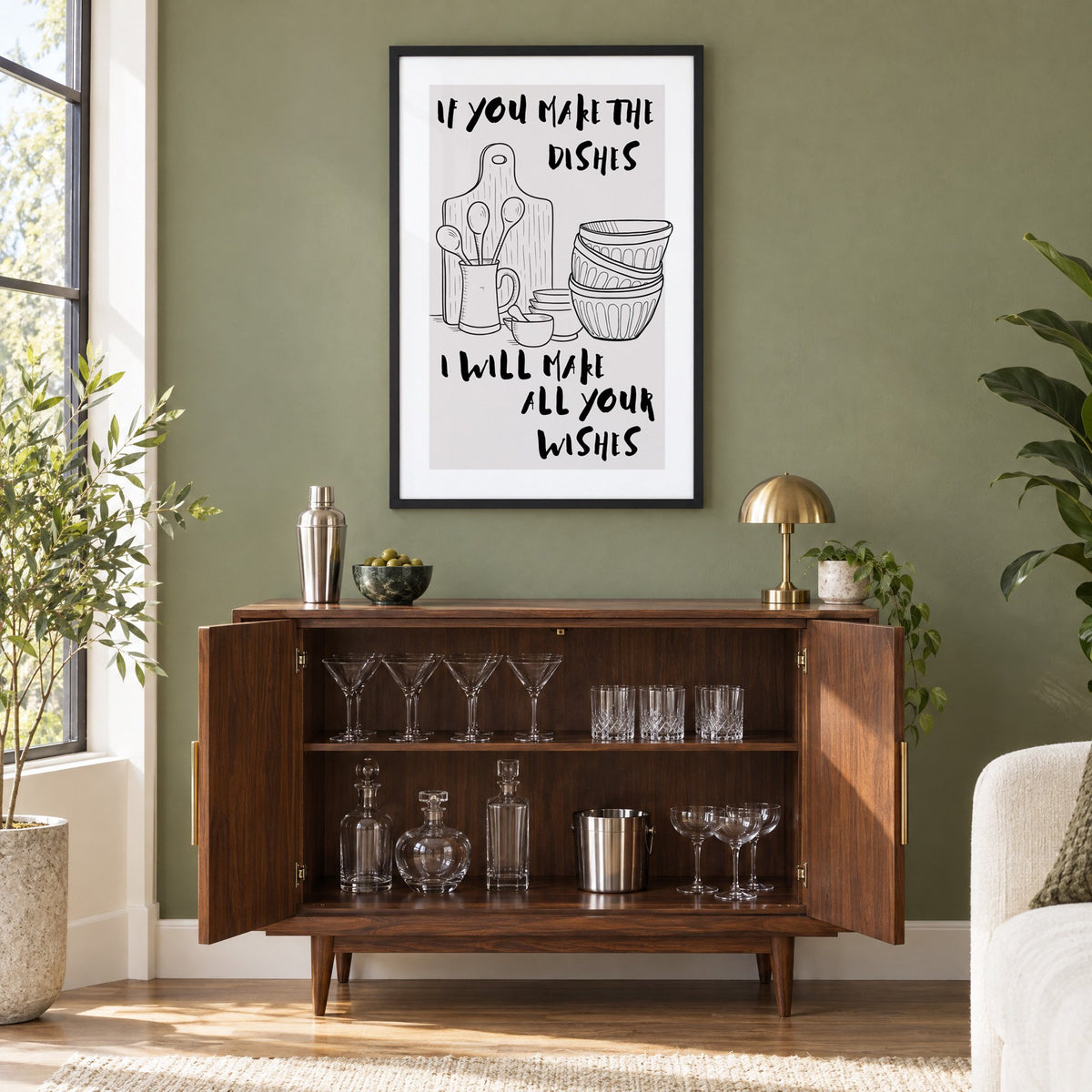 IF YOU MAKE THE DISHES kitchenware sketch print in a black frame on an olive green wall above a walnut bar cabinet with glassware