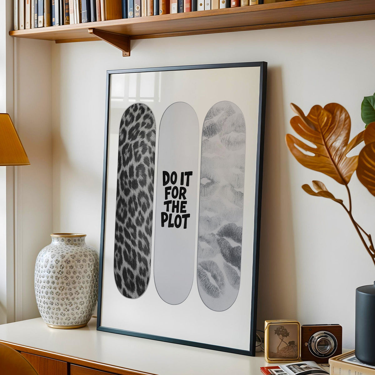 Three skateboard decks with quote and lip prints print in a black frame on a console under a bookshelf