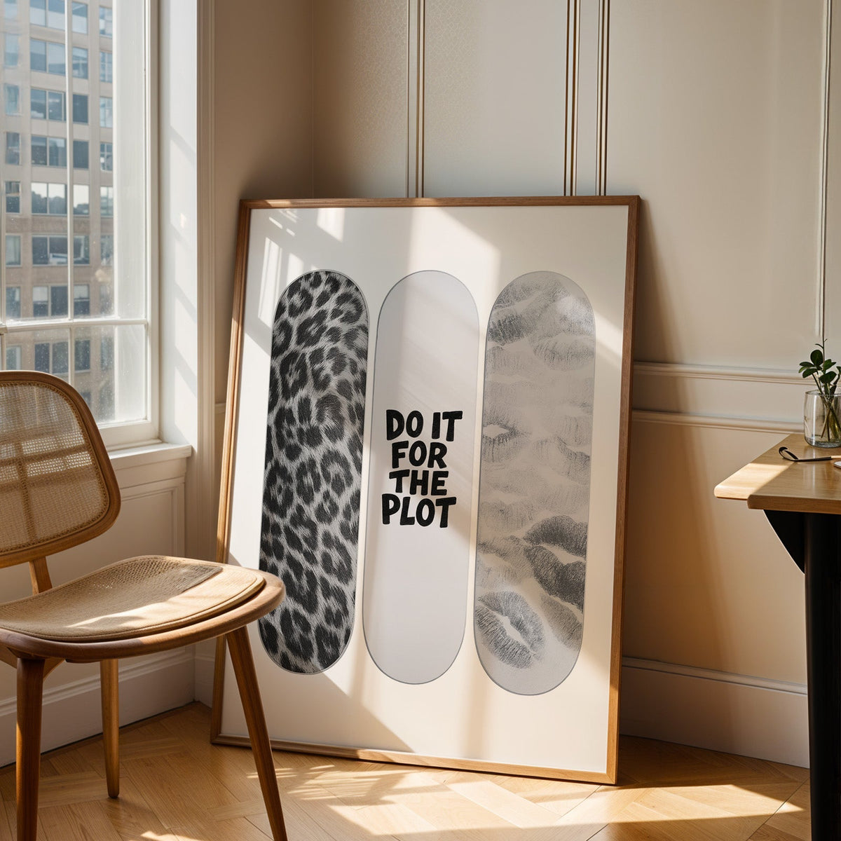 Three skateboard decks with quote and lip prints print in an oak frame leaning in a sunlit corner beside a cane chair