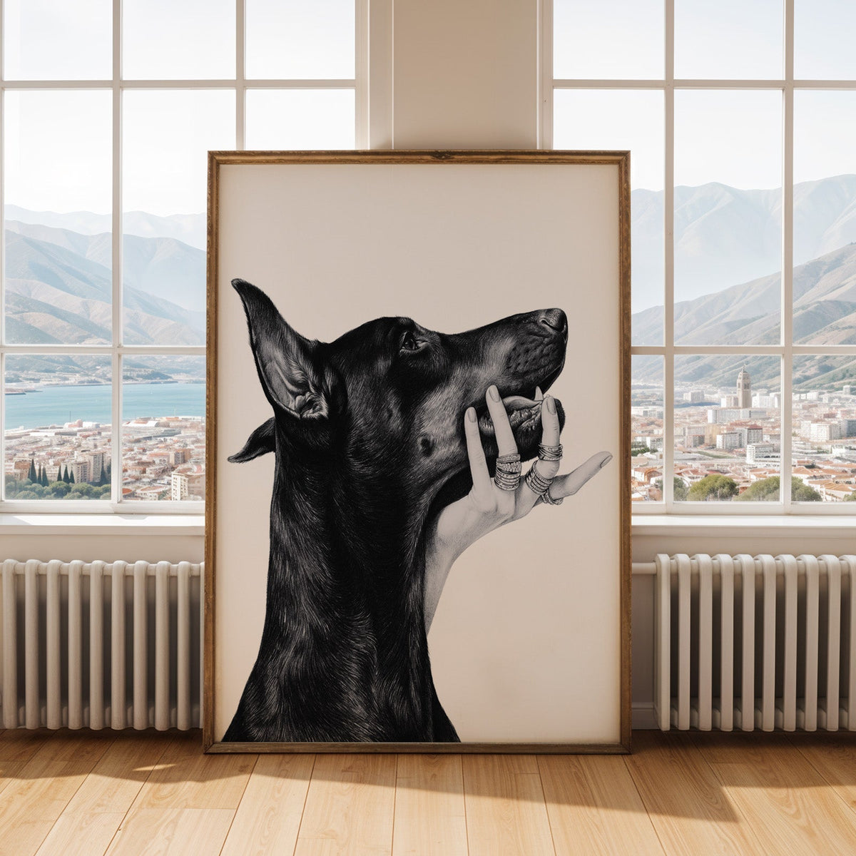 Drawn Doberman with ring-covered hand under chin print shown in an antique gold frame by tall windows with a sea view