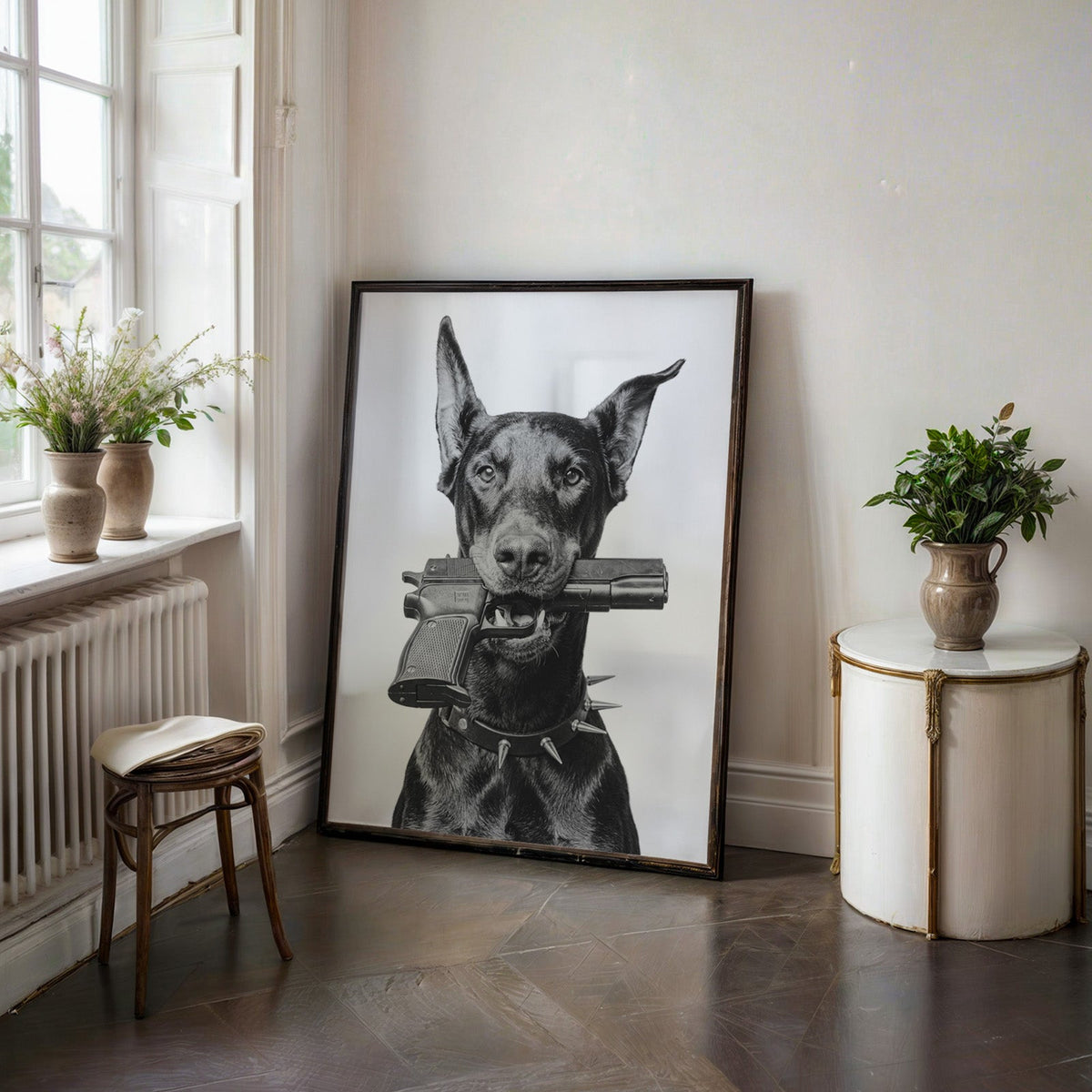 Doberman with toy pistol in mouth on white print in a black frame on a dark stone floor beside a white side table
