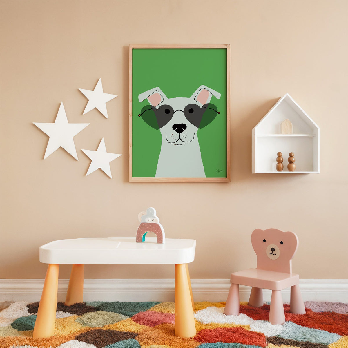 White dog in heart sunglasses nursery print in an oak frame on a peach wall above a kids table with wall stars