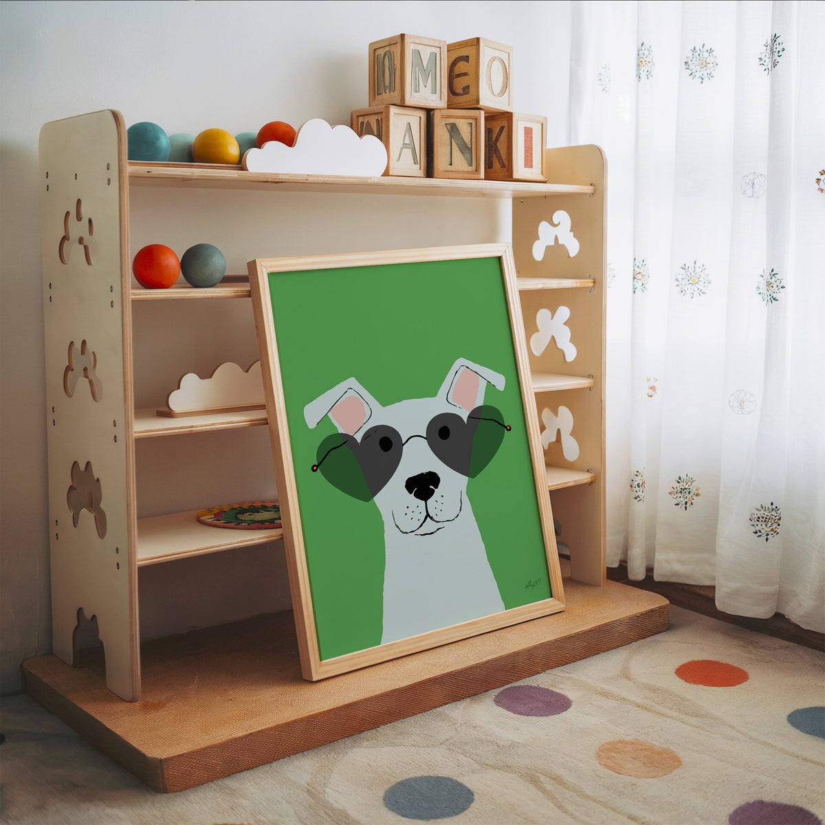 White dog in heart sunglasses nursery print in an oak frame leaning on a toy shelf with wooden letter blocks