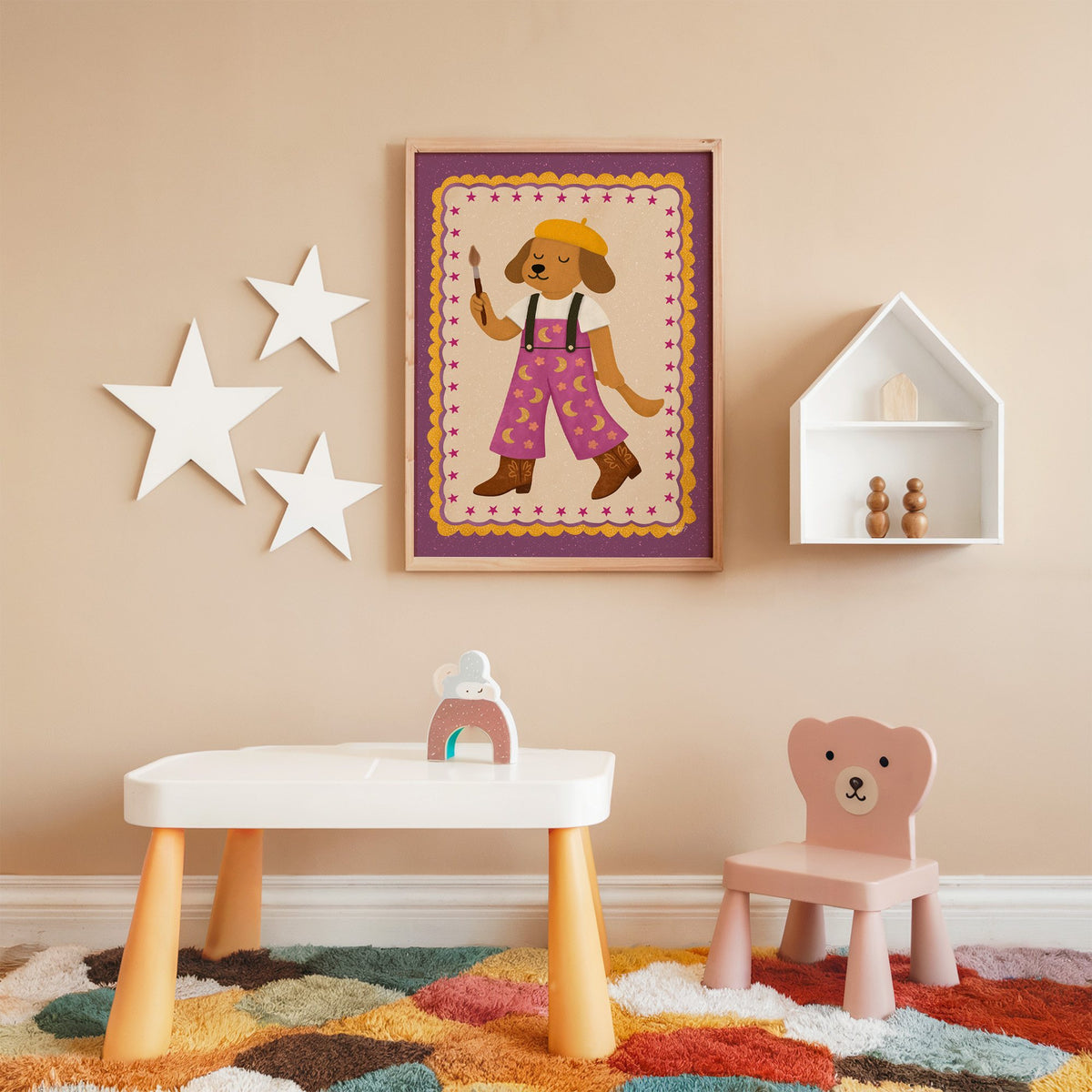 Painter dog in yellow beret nursery print in an oak frame on a peach wall above a kids table with wall stars