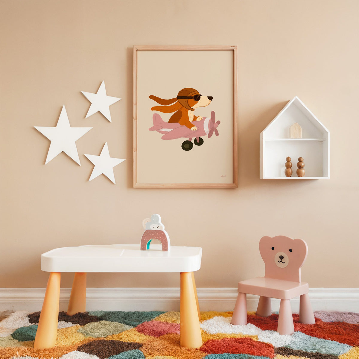 Dog pilot flying pink plane nursery print in an oak frame on a peach wall above a kids table with wall stars