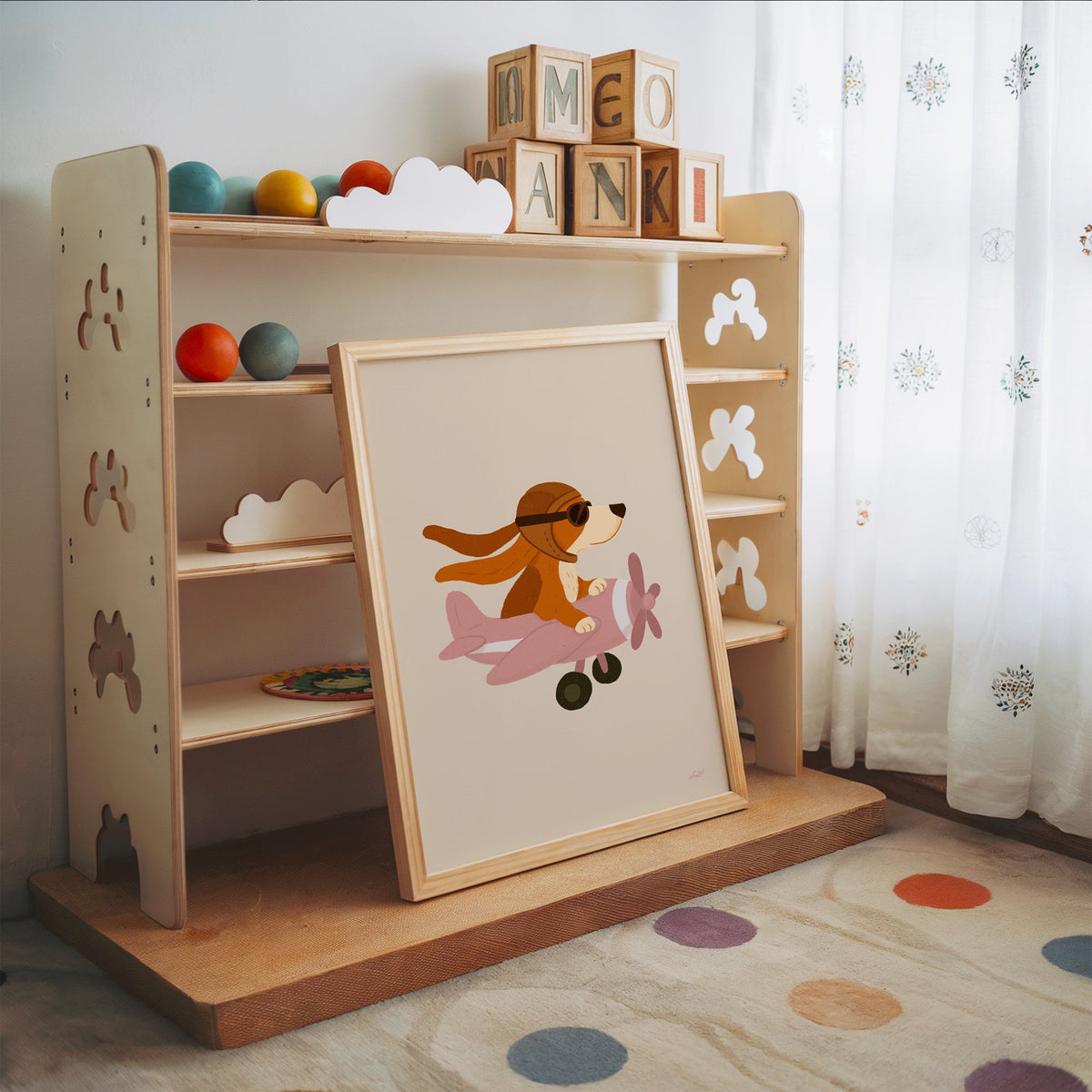 Dog pilot flying pink plane nursery print in an oak frame leaning on a toy shelf with wooden letter blocks