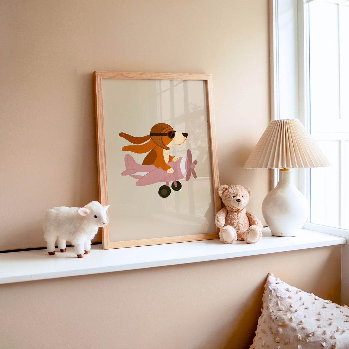 Dog pilot flying pink plane nursery print in an oak frame on a window ledge with a toy lamb and teddy
