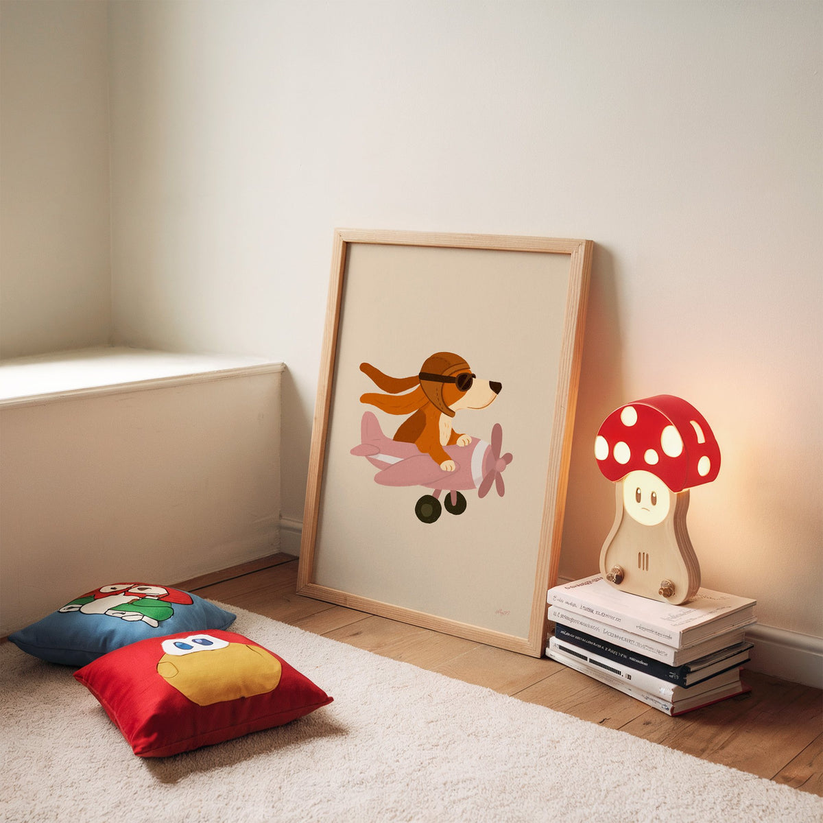 Dog pilot flying pink plane nursery print in an oak frame leaning on a rug beside a mushroom lamp and floor cushions