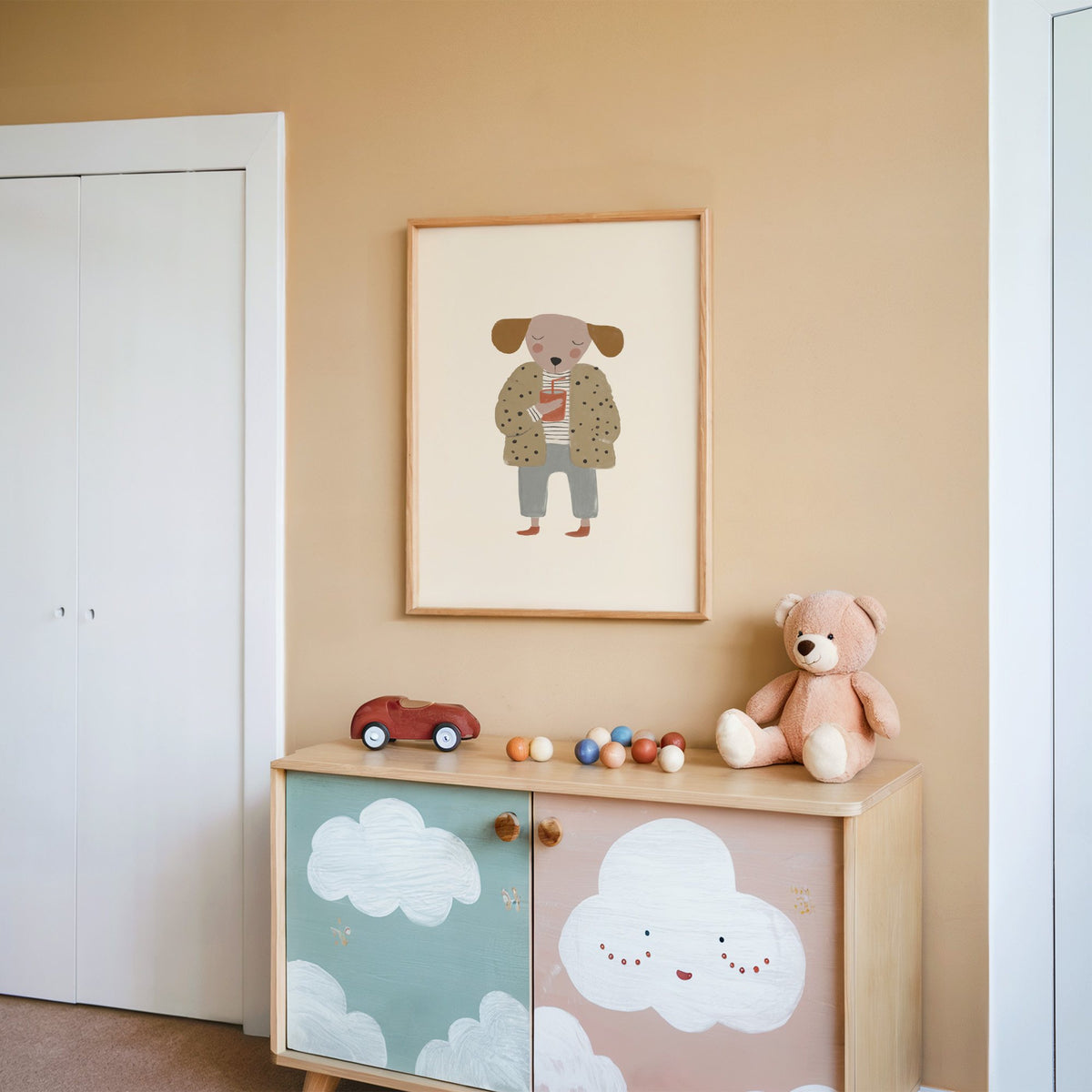 Dog in polka dot coat nursery print in an oak frame on a peach wall above a cloud-painted cabinet
