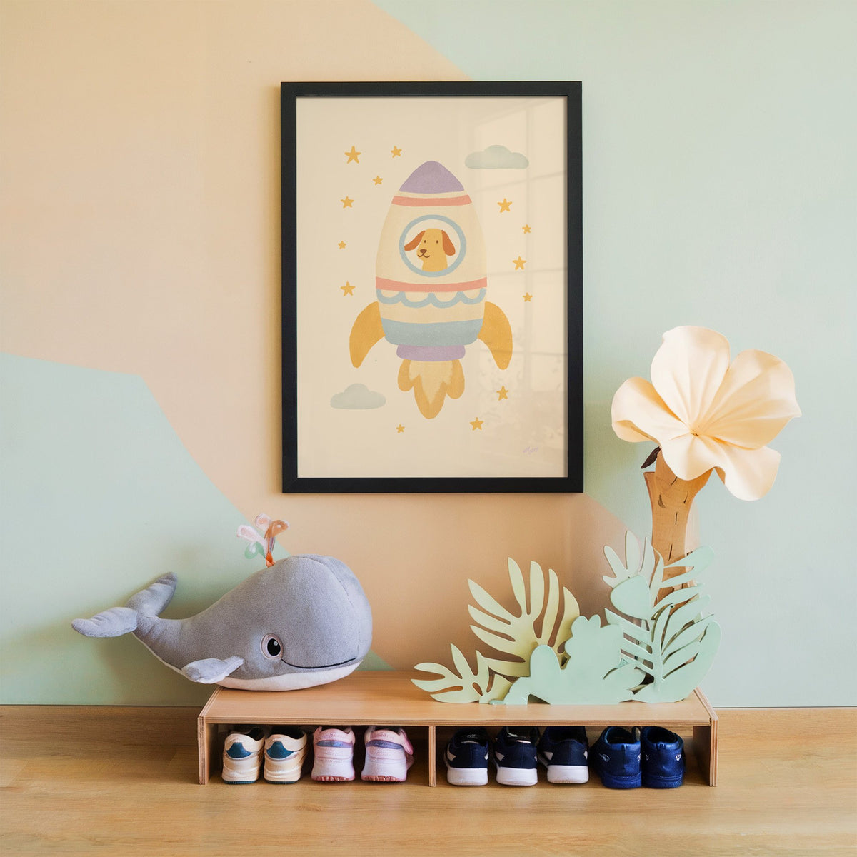 Smiling dog in pastel rocket nursery print in a black frame on a mint and peach wall above a whale plush