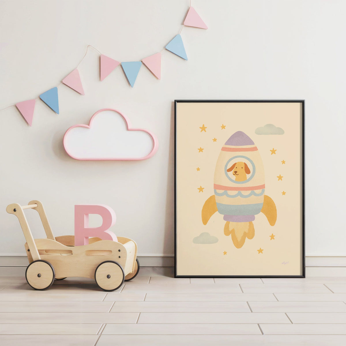 Smiling dog in pastel rocket nursery print in a black frame under pastel bunting by a wooden baby walker