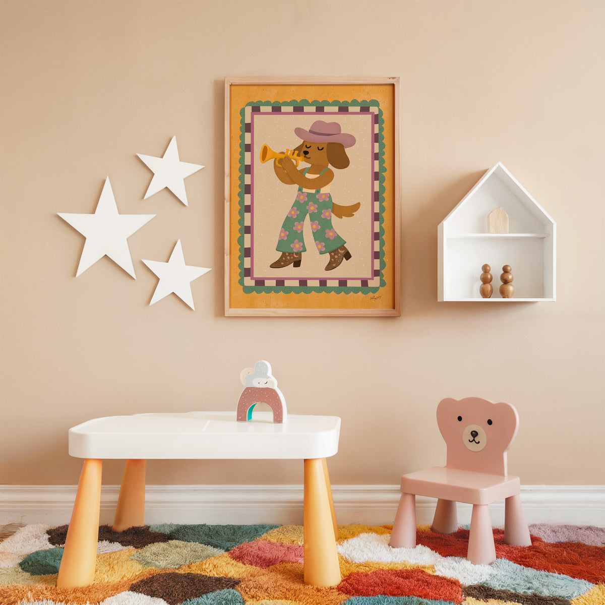 Dog playing trumpet in cowboy hat nursery print in an oak frame on a peach wall above a kids table with wall stars