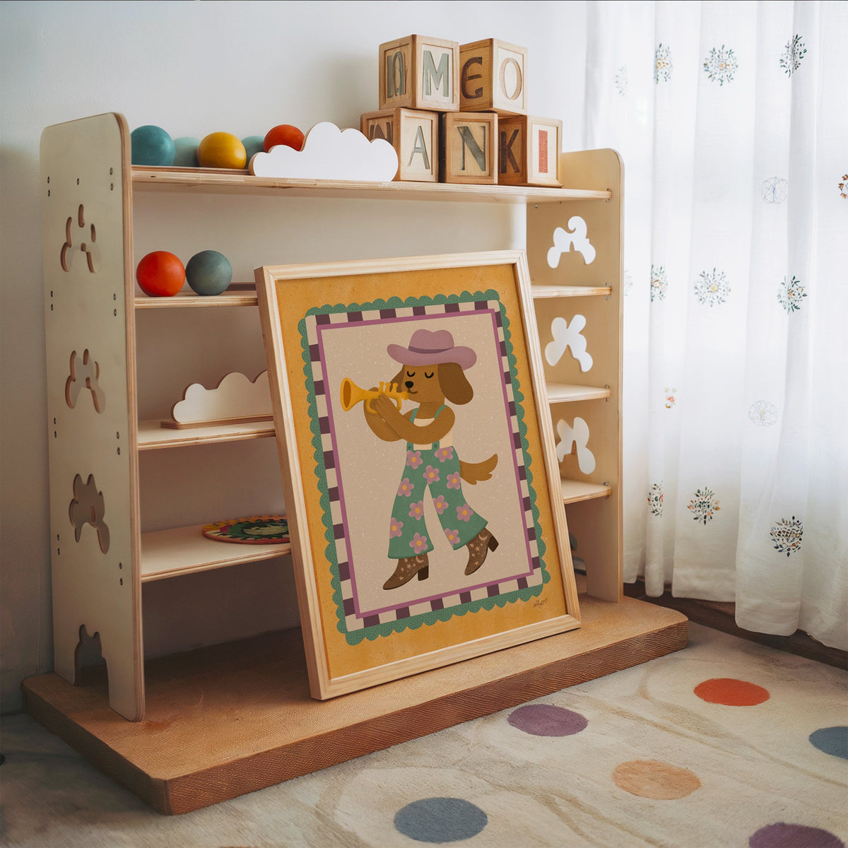 Dog playing trumpet in cowboy hat nursery print in an oak frame leaning on a toy shelf with wooden letter blocks