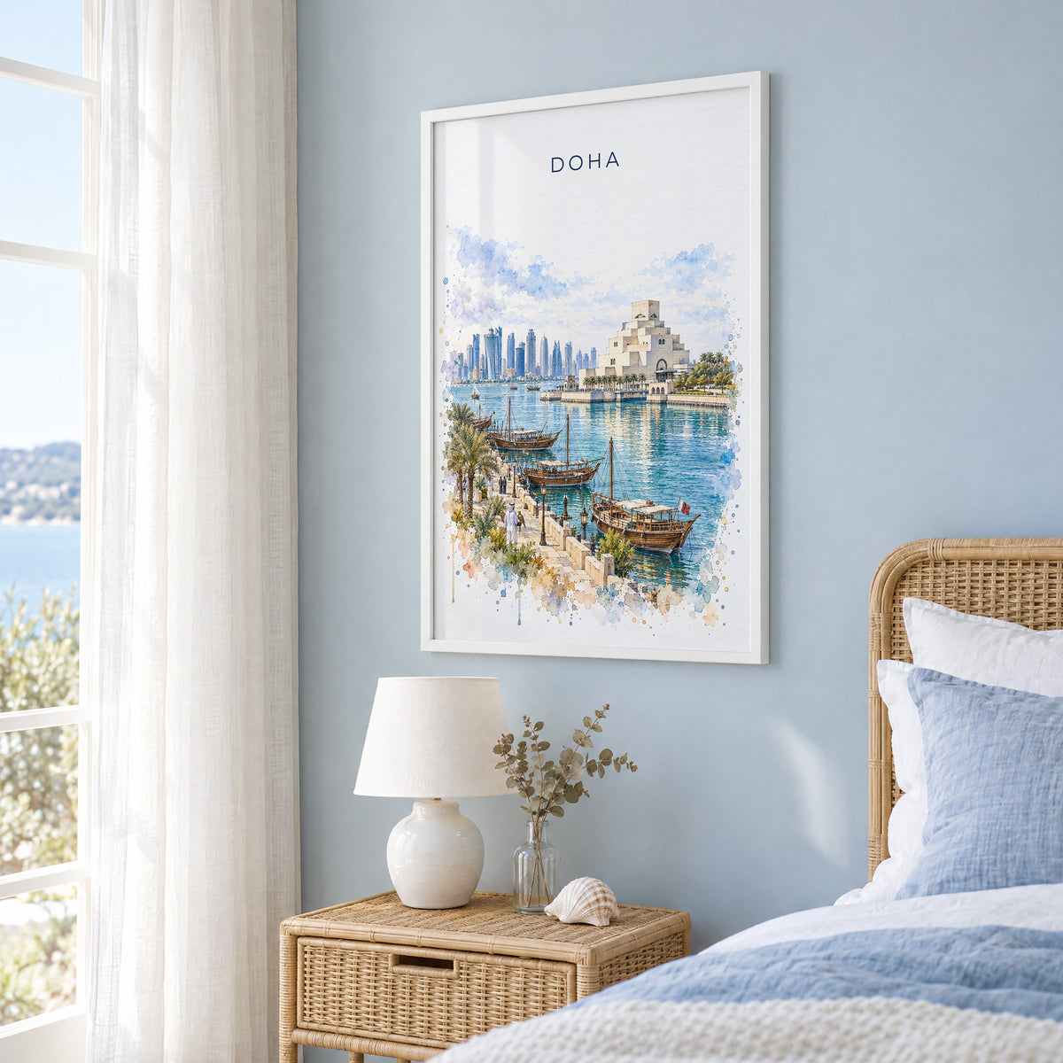 Doha watercolor print in a white frame on a pale blue wall beside a rattan bed in a coastal bedroom