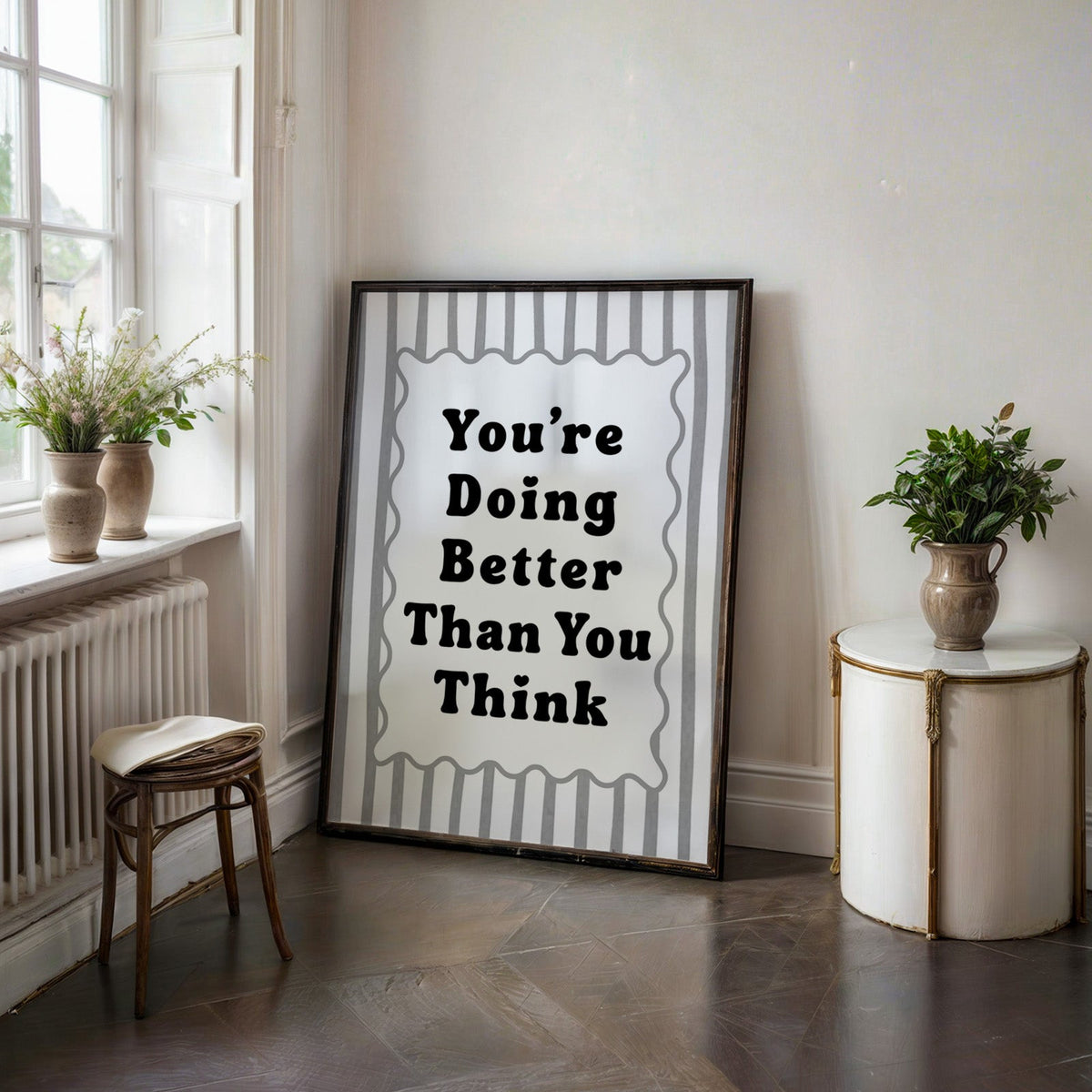 You're doing better than you think striped quote print in a black frame on a dark stone floor beside a white side table