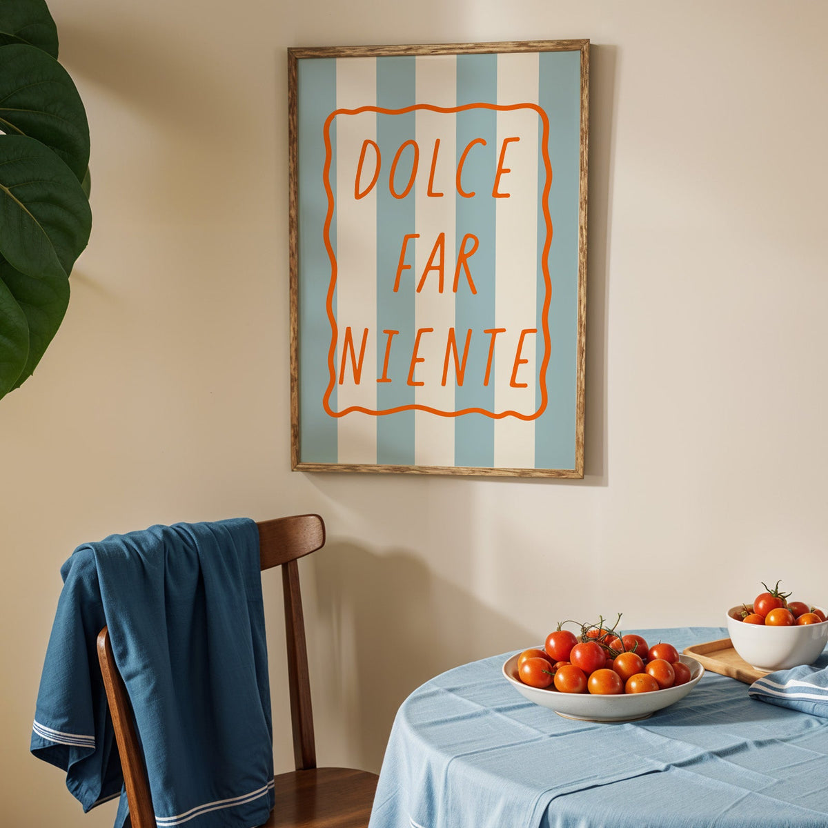 Dolce far niente print in an oak frame above a blue linen table with ripe tomatoes