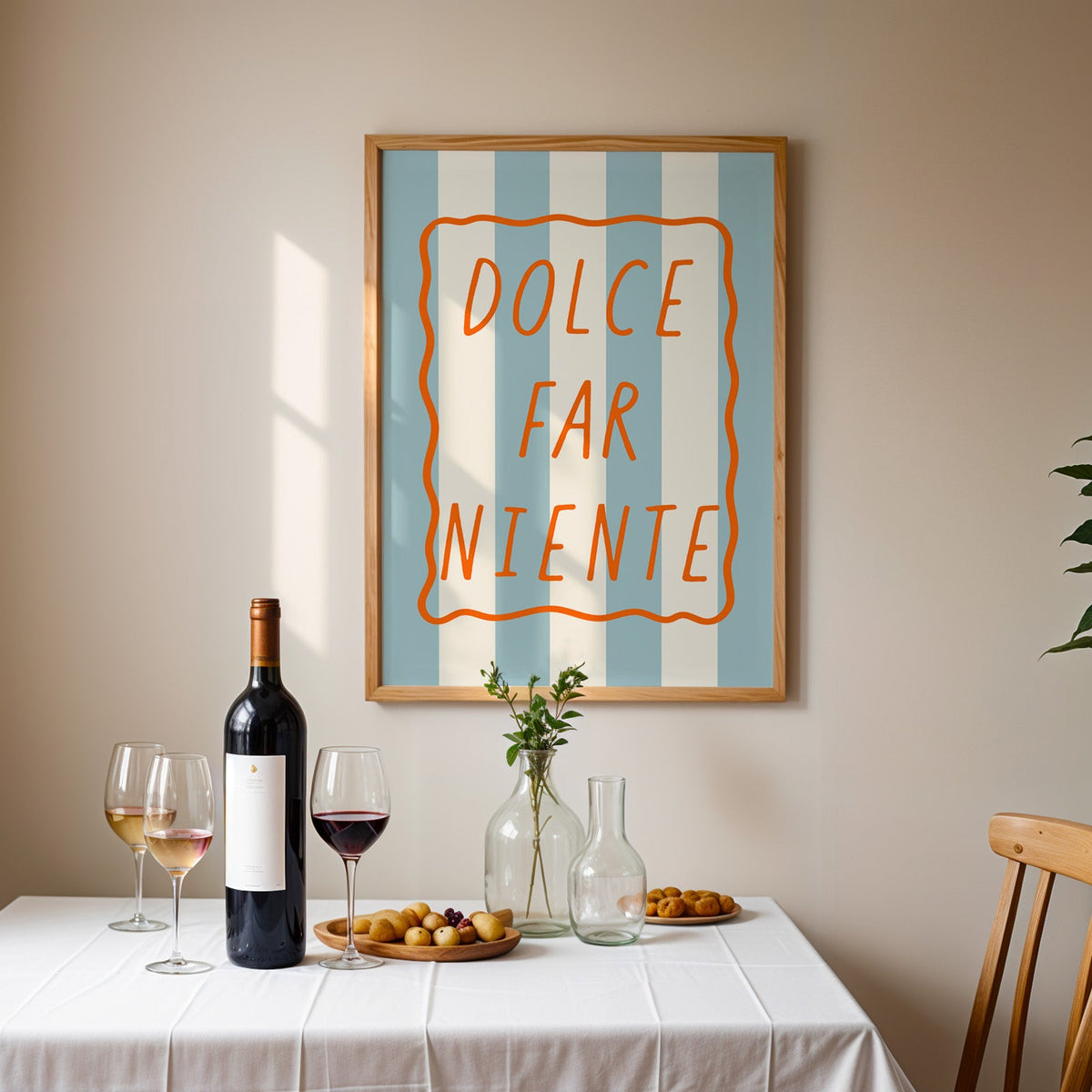 Dolce far niente print in an oak frame above a table laid with red wine and glasses