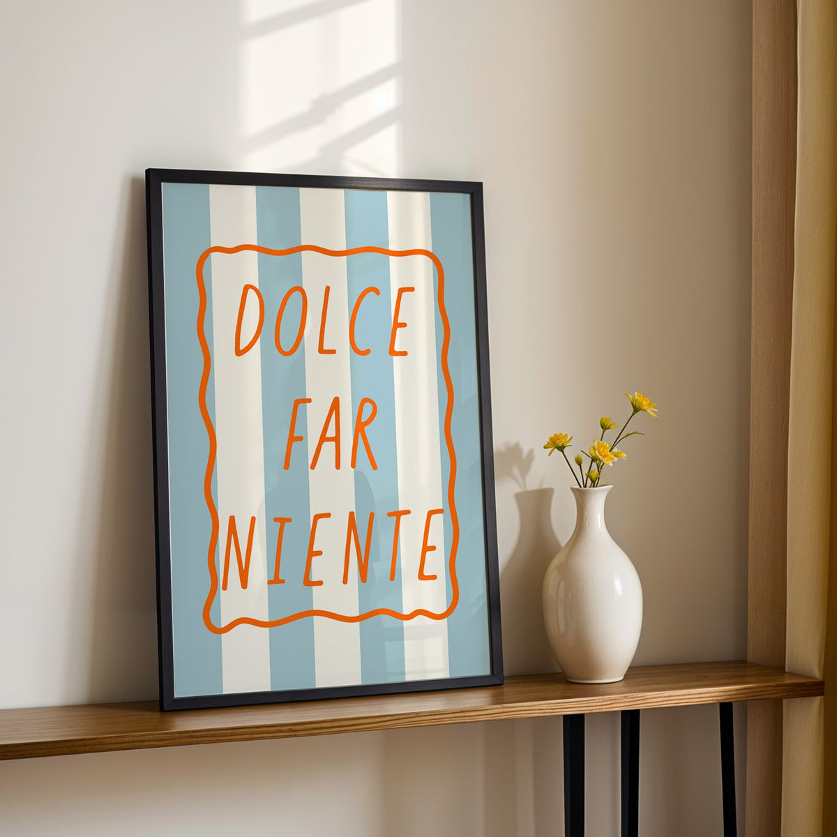 Dolce far niente print in a black frame on a console table with yellow daisies