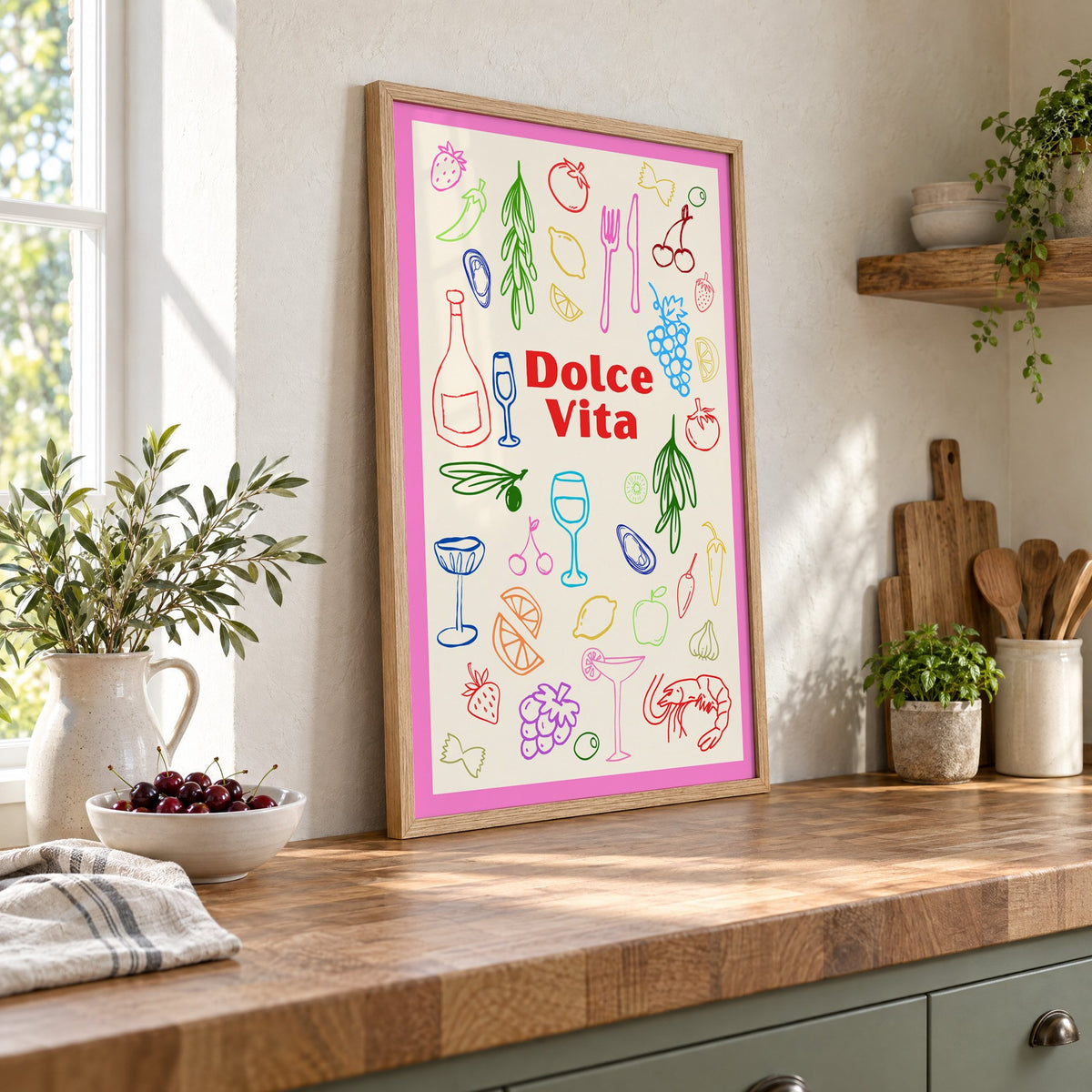 Dolce Vita colorful food doodle print in an oak frame leaning on a butcher block island beside a bowl of cherries