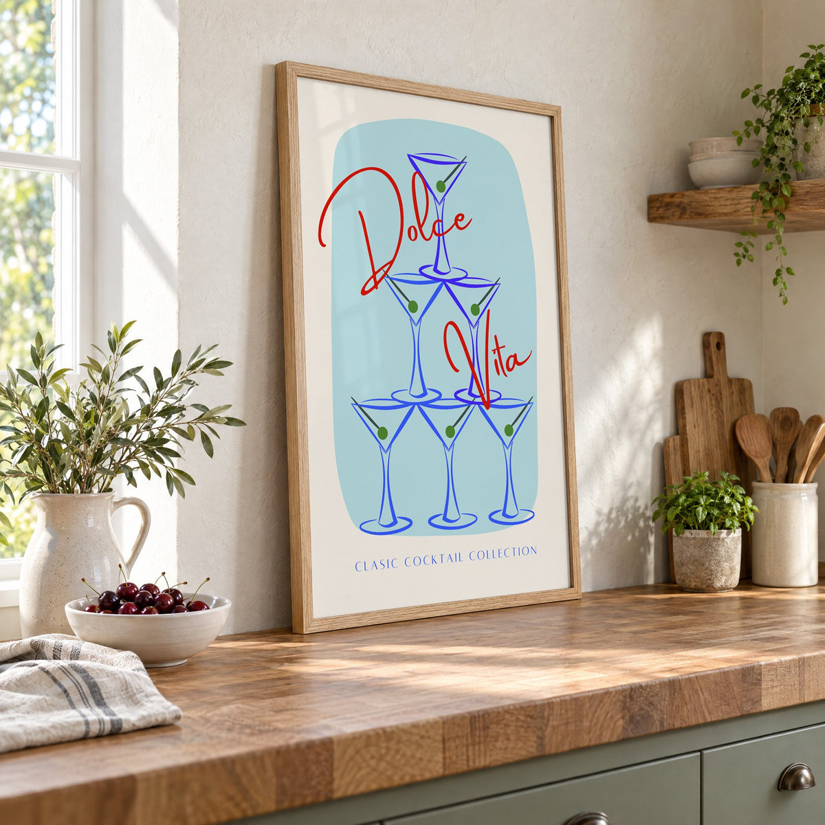 Dolce Vita martini tower print in an oak frame leaning on a butcher block island beside a bowl of cherries