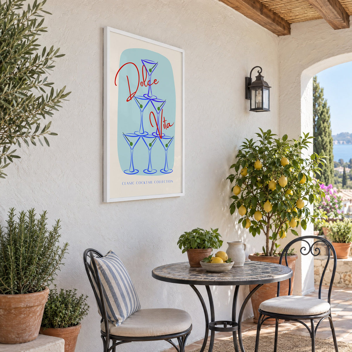 Dolce Vita martini tower print in a white frame on a sunny patio wall beside a potted lemon tree