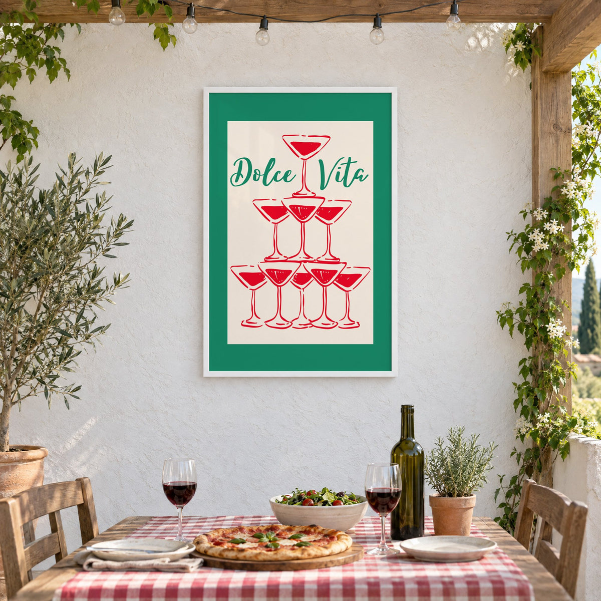 Dolce Vita red martini tower print in a white frame on a stucco wall above a checked-cloth table with pizza and red wine