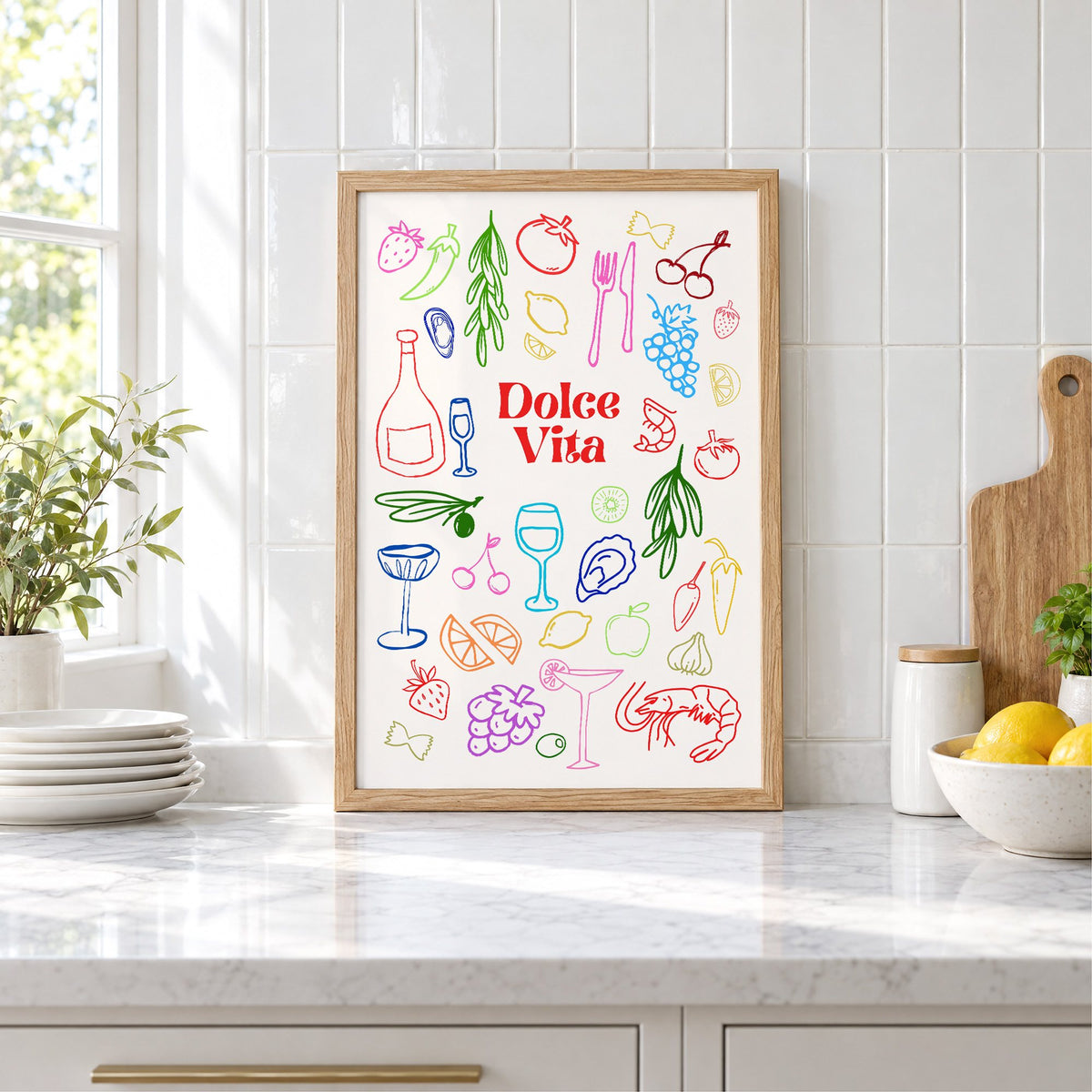Dolce Vita rainbow doodle print in an oak frame leaning on a marble counter by white tiles and lemons