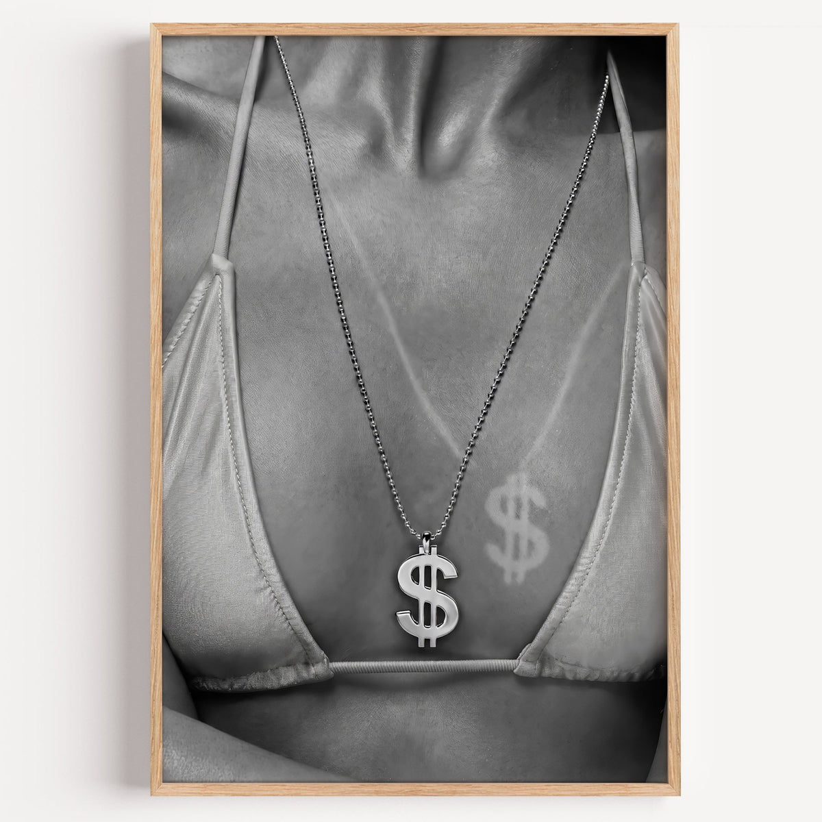Dollar sign pendant and tan line close-up print in a light oak frame on a plain white wall