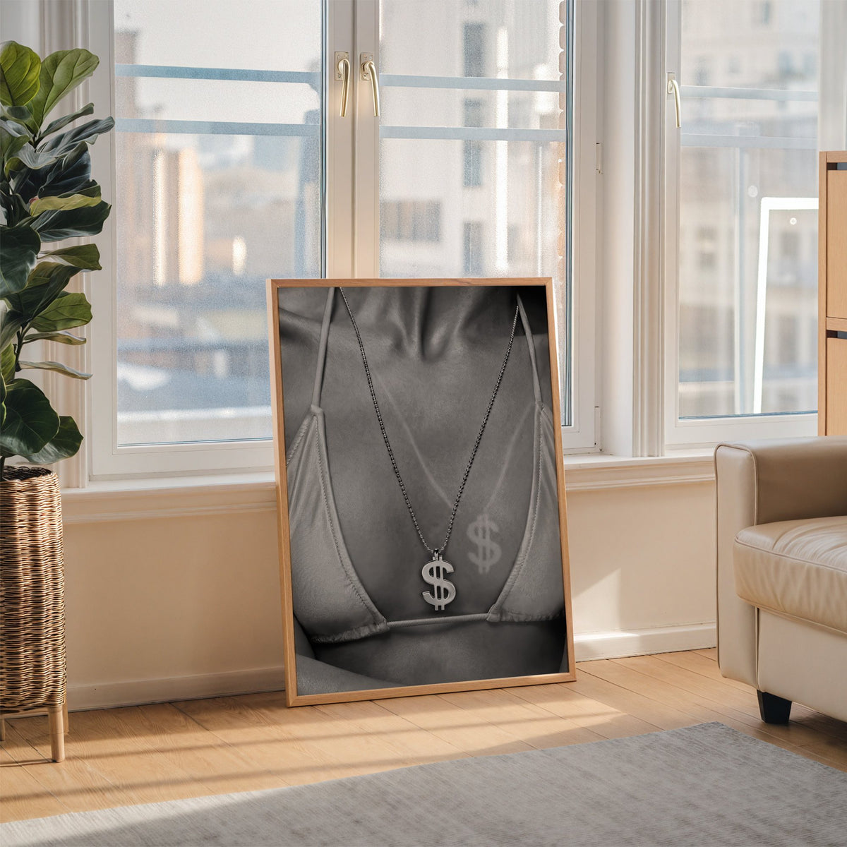 Dollar sign pendant and tan line close-up print in an oak frame leaning on the floor beside a fiddle leaf fig